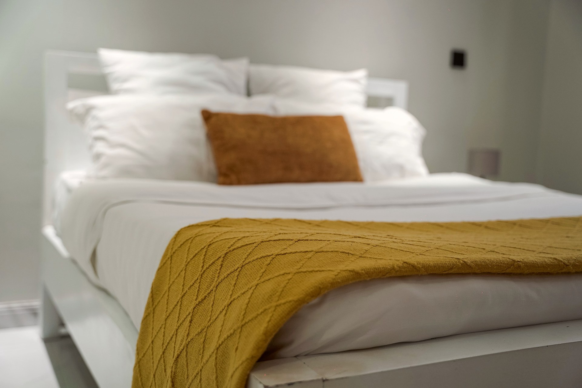 A mustard knitted throw and a rust cushion on white bedding