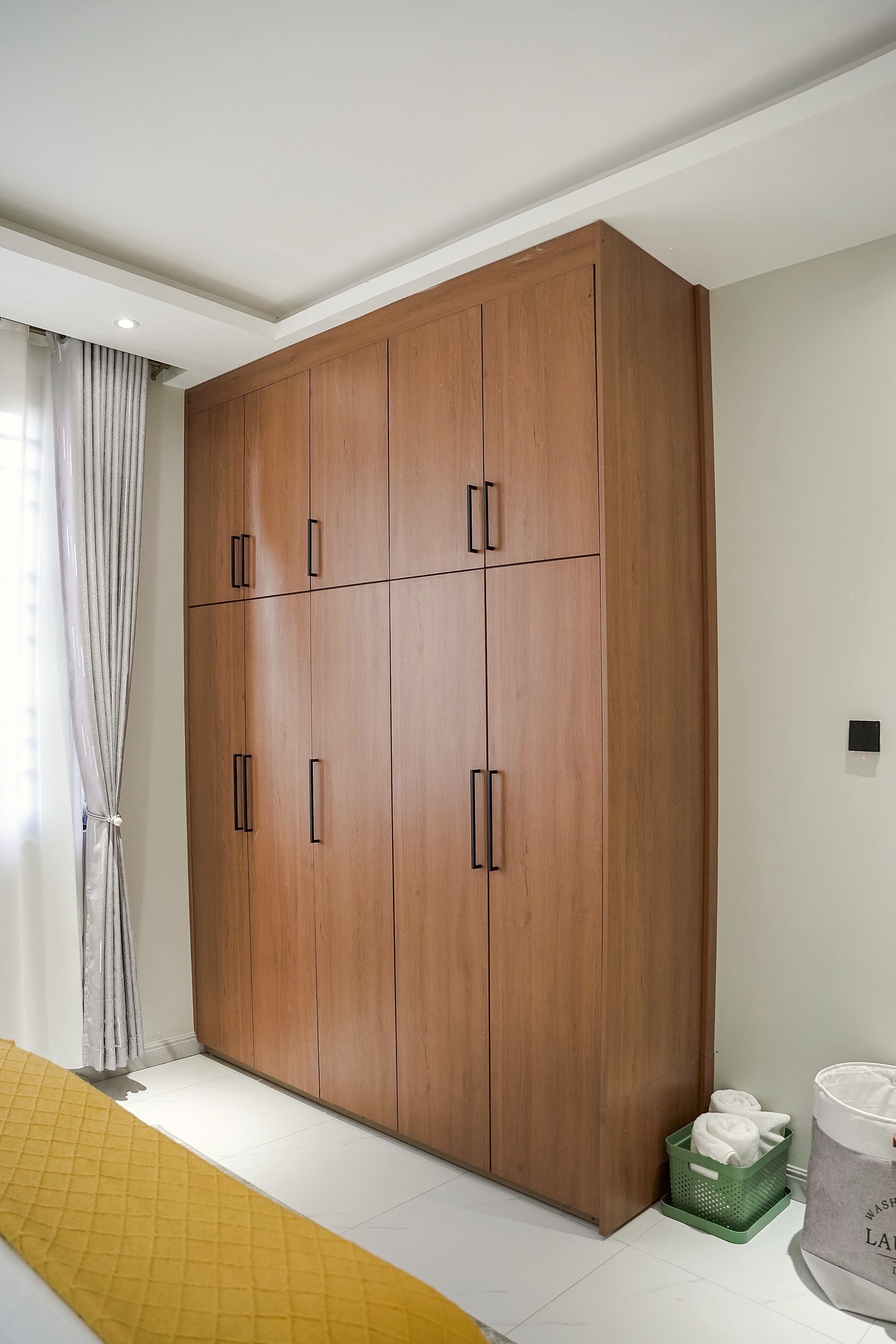 Floor to ceiling wood wardrobe beside the bedroom window