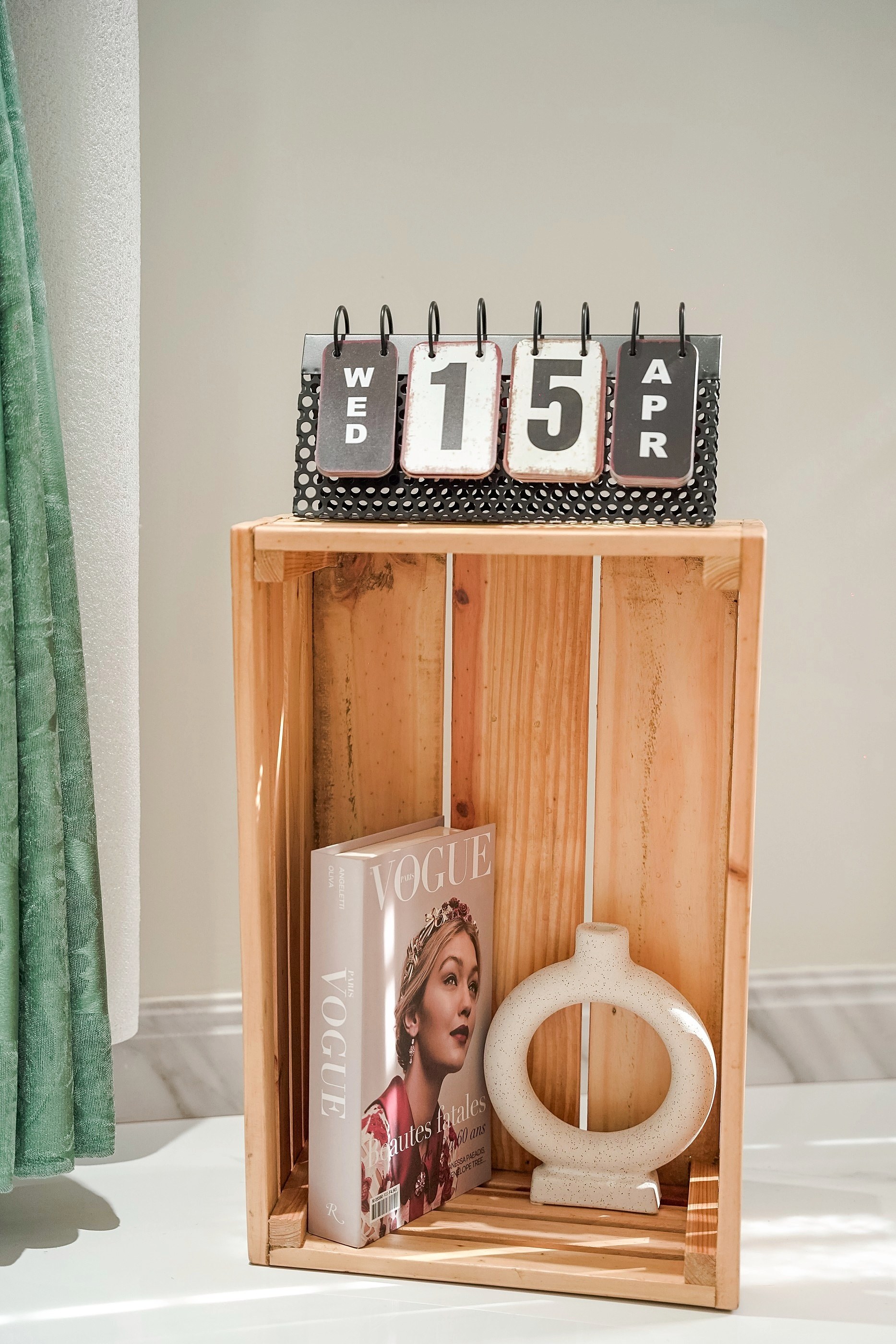 A wooden crate with a flip calendar, a magazine and a ceramic vase
