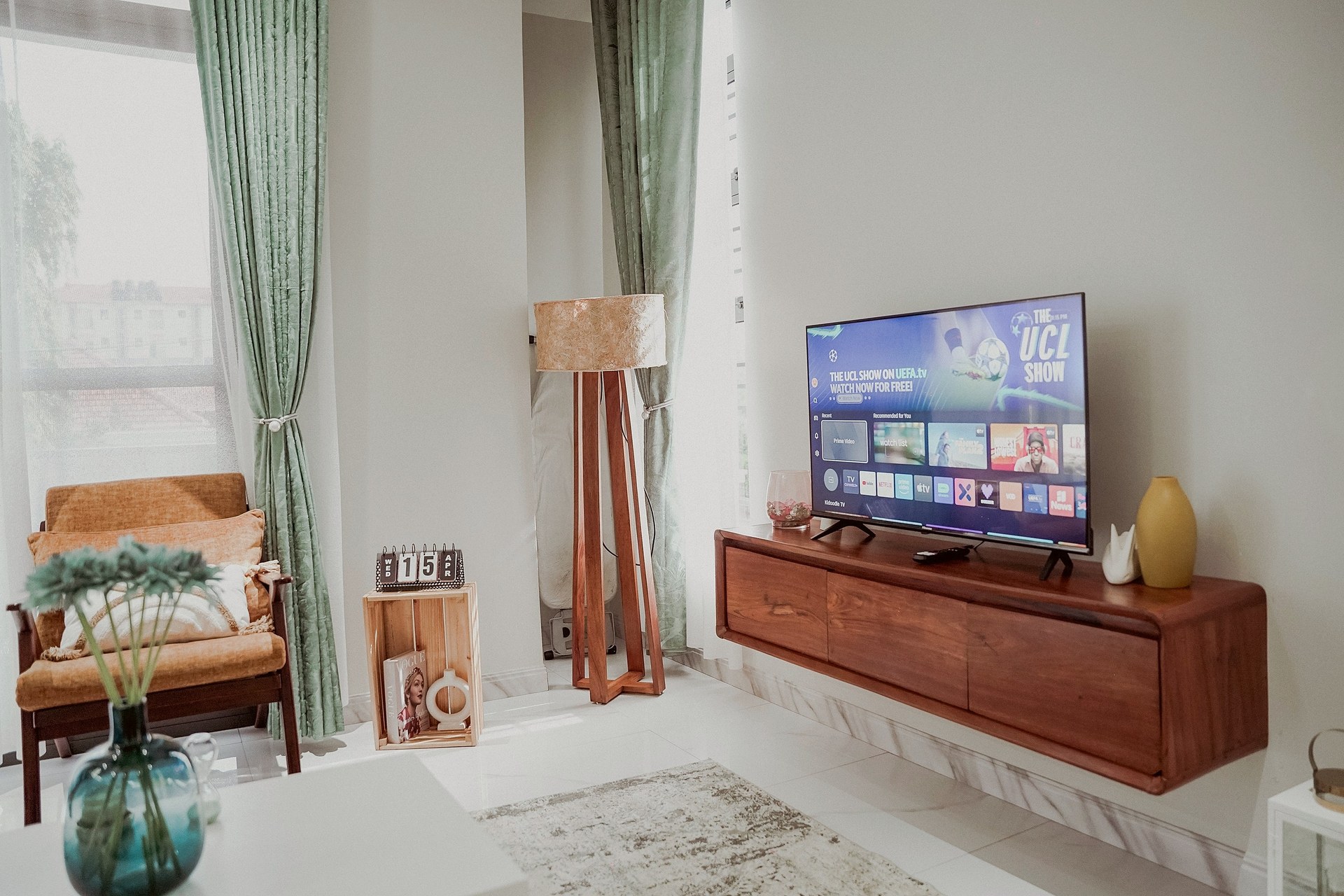 A walnut console beneath the television by the green curtains