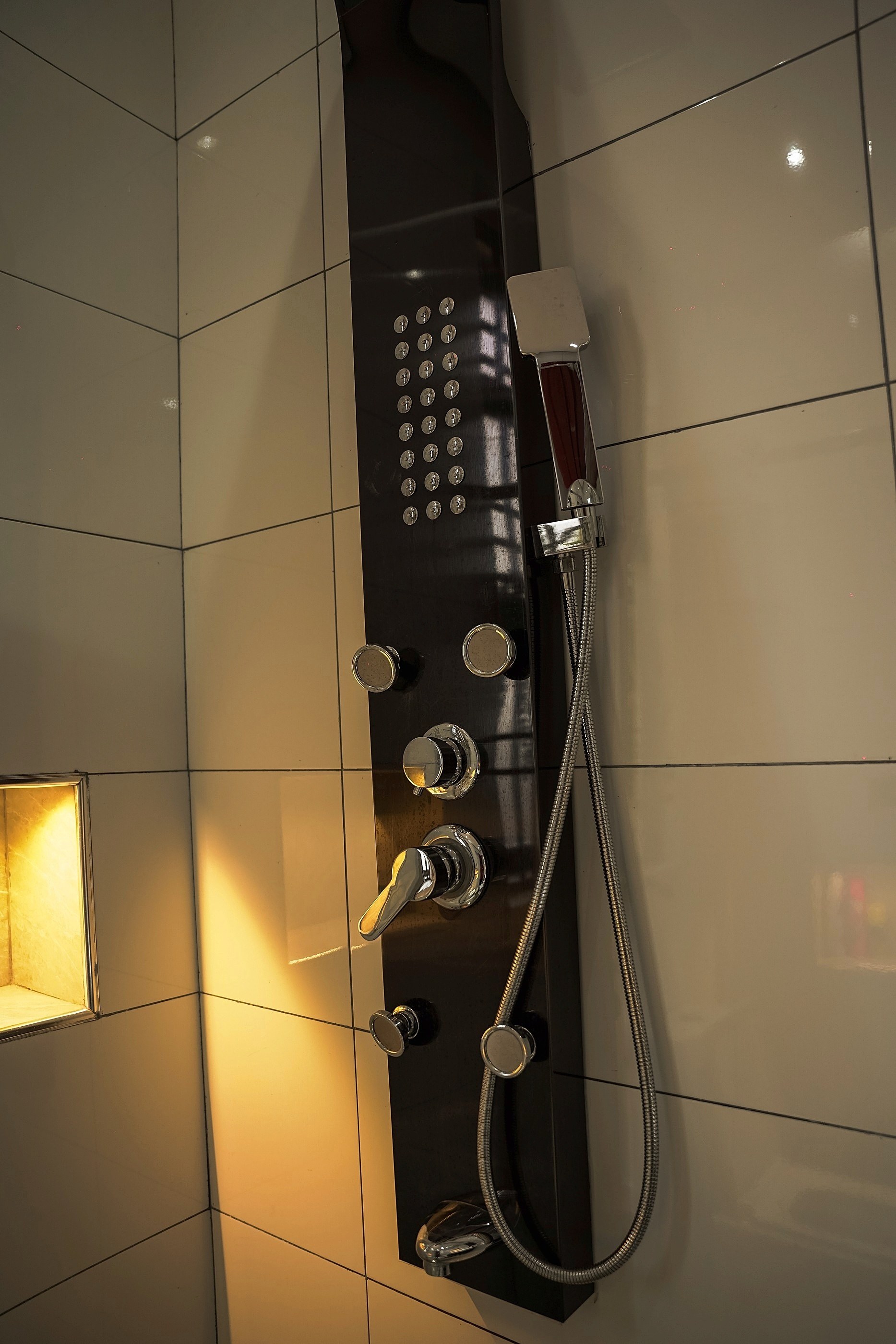 The black shower panel lit warm against white tiles
